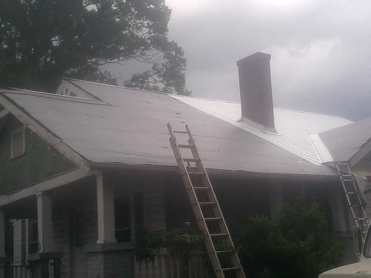 Ladders against a metal roof on an older home with a brick chimney in Fenton