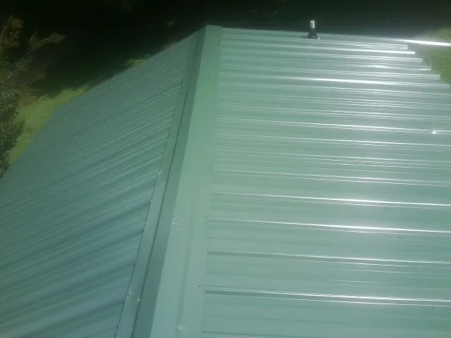 New green metal panels meeting at the ridge of a roof — Flat Roof Repair work by our crew in Fenton