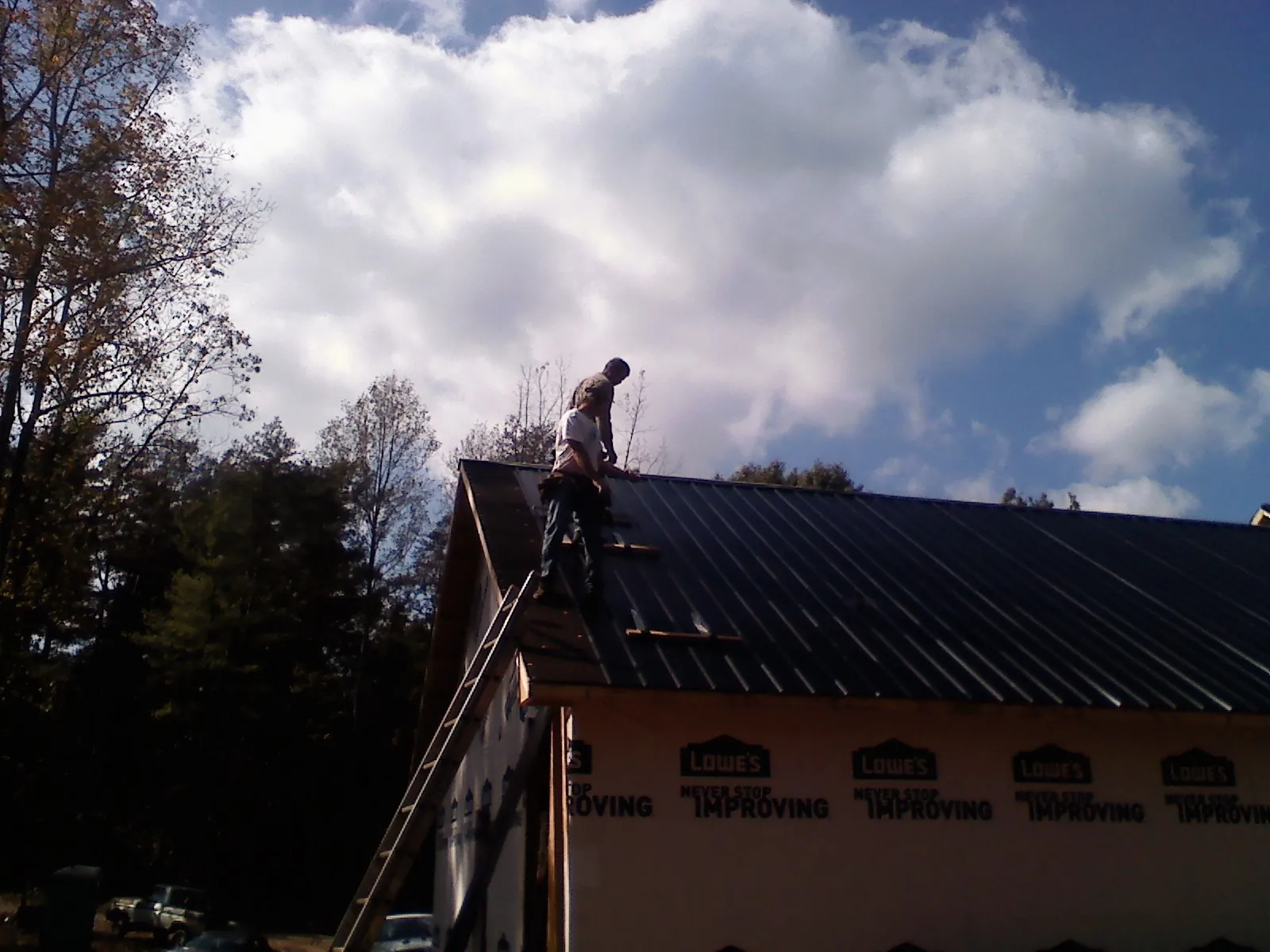 Roofer fastening dark metal panels high against a cloudy sky, from a Roof Inspection job in Fenton