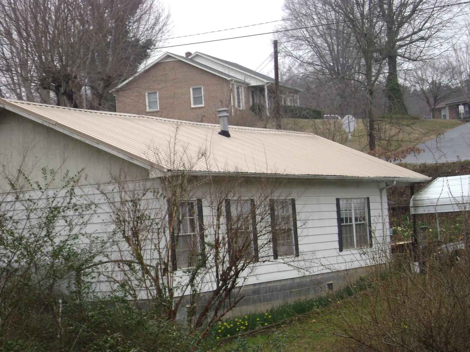 Tan metal roof on a white sided house set into a hillside — Commercial Roofing by Roofing Brothers in Fenton